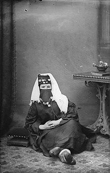 Margaret Jones poses for a portrait. She is wearing a loose black outfit and a decorated head covering that shows only her eyes.