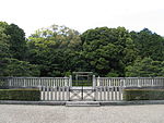 Torii gate behind two concrete fences. In the background there are trees.