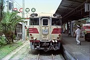 Diesel train stopped at platform with buildings to the side