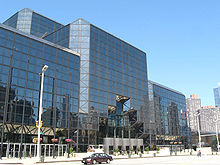 A building of dark tinted glass stands over a city street. The corners of the building are smoothed at 45-degree angles.