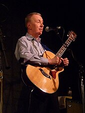 A grey-haired man holding a guitar