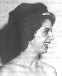 A smiling young white woman with dark curly hair and dark eyebrows; her shoulders are bare because she is wearing a strapless gown (out of frame)