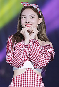 Nayeon smiles and forms her hands into a heart