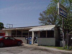 White single story building with a red car parked in front, also the restaurant's sign at photo right