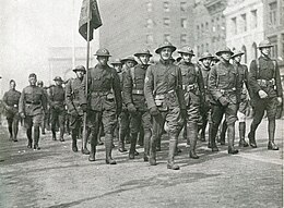 Black and white photo of soldiers lined up and marching in a street