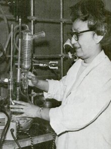 A middle-aged Chinese woman wearing a lab coat and glasses; she is working with chemistry laboratory equipment.