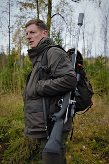 A photograph of Paul Childerley walking in the woods with a rifle