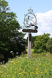 Metal wire sign labeled "Piltdown" with golfer, geese and skull with