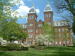 A red brick building with a mansard roof and two identical towers at the top surrounded by trees
