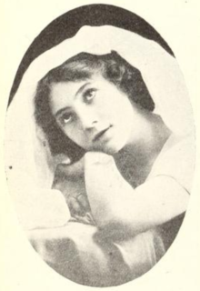 A young white woman with dark hair, chin resting on one hand, a white cloth covers the top of her head