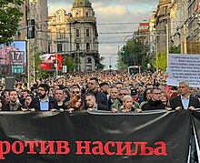 Aleksandar Jovanović Ćuta walking with demonstrators in Belgrade while holding a banner that says Serbia Against Violence