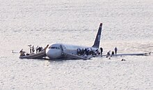 A partially submerged Airbus A320 with front emergency slides deployed and people standing on its wings
