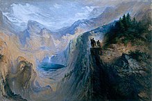 两个人站在悬崖上，俯瞰森林和高大山脉环绕的山谷。