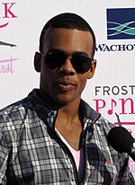 A young black man with short black hair, wearing sunglasses and a gray-and-white checked shirt.