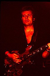 A red tinged photograph of John Paul Jones playing a bass guitar
