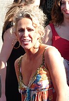 Woman with blonde hair wearing a multi-coloured dress and golden hoop earrings smiling