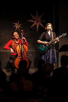 Photograph of the sisters; Aubrey on the left playing a cello and Laser on the right playing a guitar.