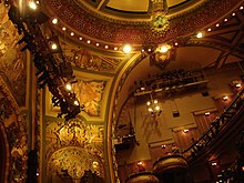 A side view of the balcony-level seats, looking up from the orchestra level. There are murals on the walls.