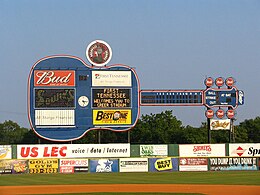 A view of a giant blue guitar-shaped scoreboard beyond the left-center field wall. Advertisements for local businesses adorn the guitar and the green outfield wall below.