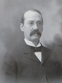 A black and white portrait of Charles W. Anderson. He is wearing a suit, a bowtie, and glasses. He is facing to the right.
