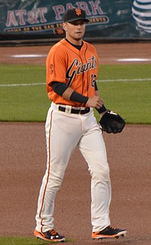 A man in an orange baseball jersey, white pants, and a black cap