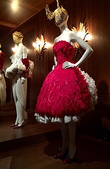 Two dresses on mannequins. On the left, a white dress with ruffles around the waist. On the right, a red sleeveless, strapless dress with a cinched waist and very full skirt.