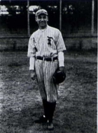 A man in a light baseball uniform with dark pinstripes standing on a field with a glove on his left hand