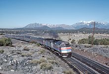 Two locomotives leading several railcars through the desert