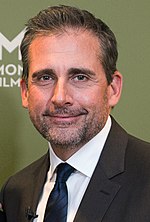 A man with black hair, Steve Carell, is standing in a tux. He is looking towards the camera and smiles.