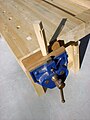 A bench vise with its dog extended, holding (without using the dog) a wooden bench dog being worked.