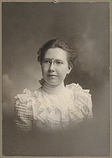 Young white woman in 1902, wearing a lacy high-necked white blouse and pince-nez eyeglasses.