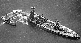 Aerial photo of a fireboat hosing down the stern of a battleship.