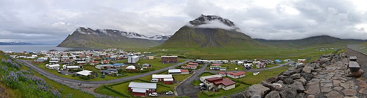 The small seaside town of Bolungarvík sits in front of steep green mountains, with their tops obscured by clouds.