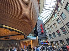 A large museum atrium featuring a large wooden bowl-shaped structure suspended from the ceiling