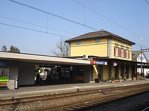 Two-story yellow station building with hip roof and canopy-covered platforms