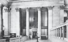 Black-and-white photo of the building interior, with the teller's desk on the right and a doorway with a pair of columns in the background