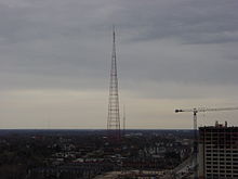 At dusk, a silhouetted, unlit TV tower looms over the Kansas City skyline as seen from the air.