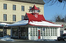 A white building with a red pointed and flared roof covered in snow.