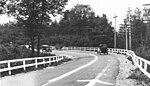 A grayscale view of a rural two-lane road lined with fences and telephone poles