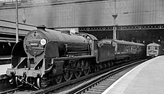 A steam locomotive waiting with its train at a station