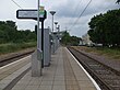 A set of two tram tracks with a platform in the middle. There are shelters and a ticket machine on the platform.