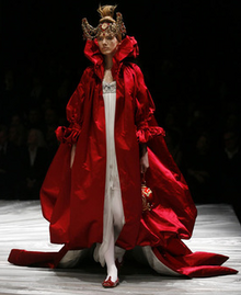 A woman wearing a white dress under a red satin robe with an exaggerated high collar.