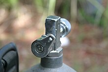 A yoke style cylinder valve is shown, with the outlet directly above the centreline and the chrome-plated brass knob and reserve lever on opposite sides in the same plane.