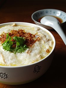 Bowl of creamy white porridge with some toppings; a spoon and dish of sauce sit in background