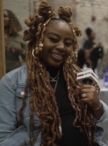 The woman, Pinky Cole, has brown skin and dyed red locs and is smiling at the camera.