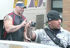 Two adult Hispanic males wearing hats posing for a photograph.