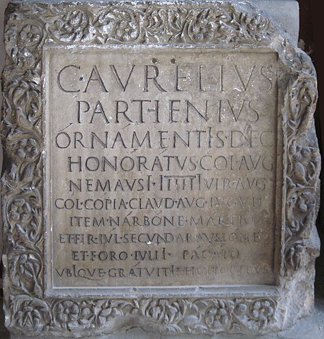 A square block of stone with a Latin inscription and a floral border.