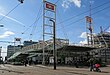 A tram is approaching in the distance on the right near a train station, with three British Rail Double Arrows visible on signs at the top.