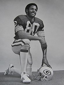 Lofton posing in uniform kneeling with his hand on his helmet