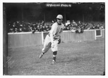 A man in a light baseball uniform with a dark "P" on the left breast having just tossed a baseball infront of a grandstand